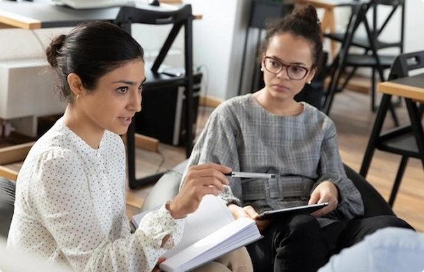 Twee vrouwen in gesprek tijdens een commissiebijeenkomst van DUFAS-FRIS, zittend in een informele werkomgeving.