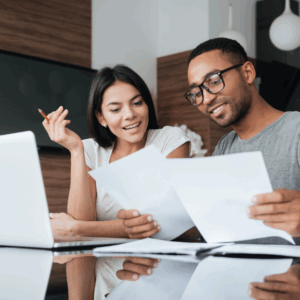 A man and a woman happily reviewing documents together at a desk with a laptop.