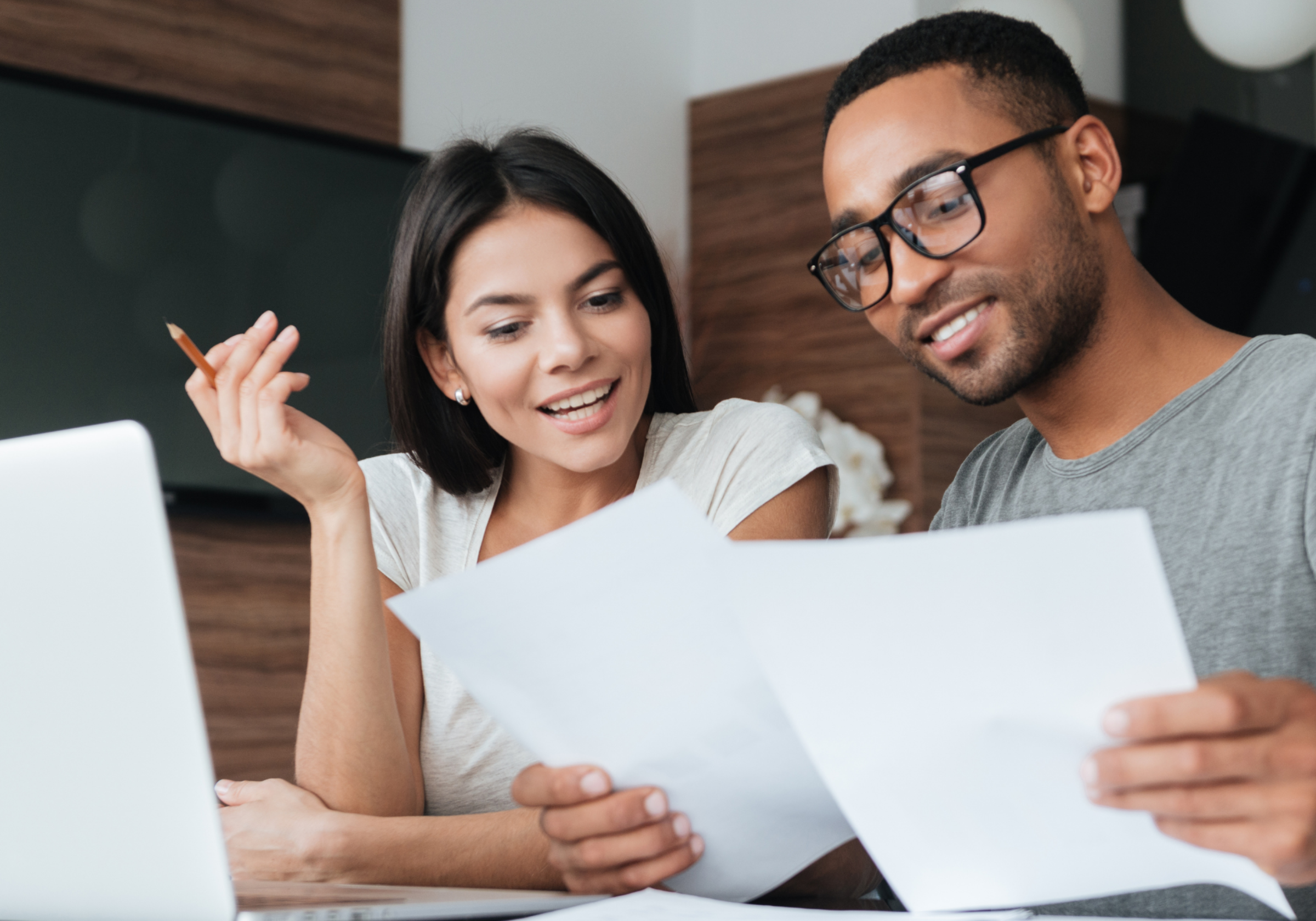 A man and woman happily review documents together at a desk with a laptop.