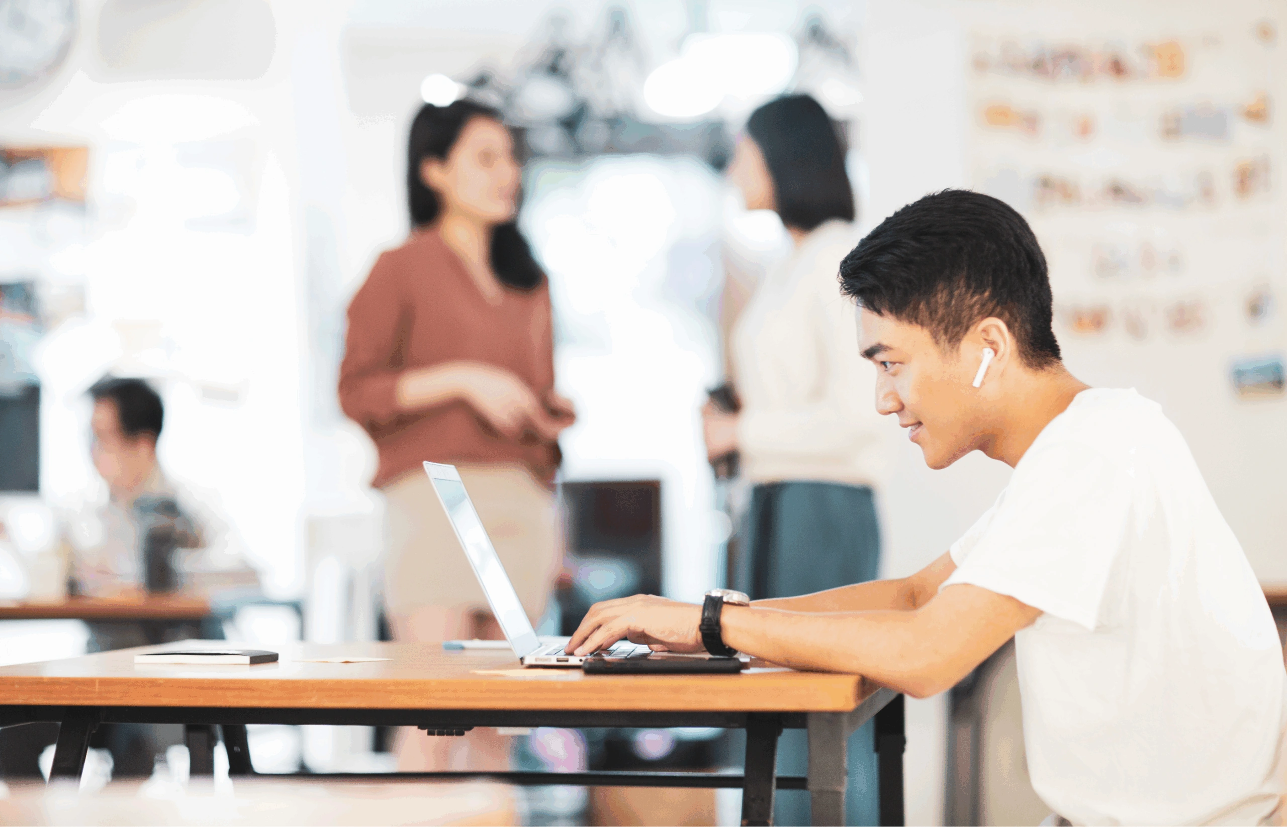 Jonge man werkt gefocust op zijn laptop in een moderne, open werkomgeving met collega's op de achtergrond.