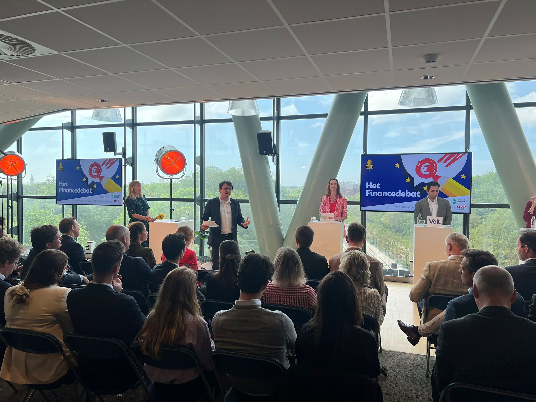 Publiek kijkt naar sprekers op het podium tijdens Het Financiedebat 2024 in een moderne zaal met grote ramen.