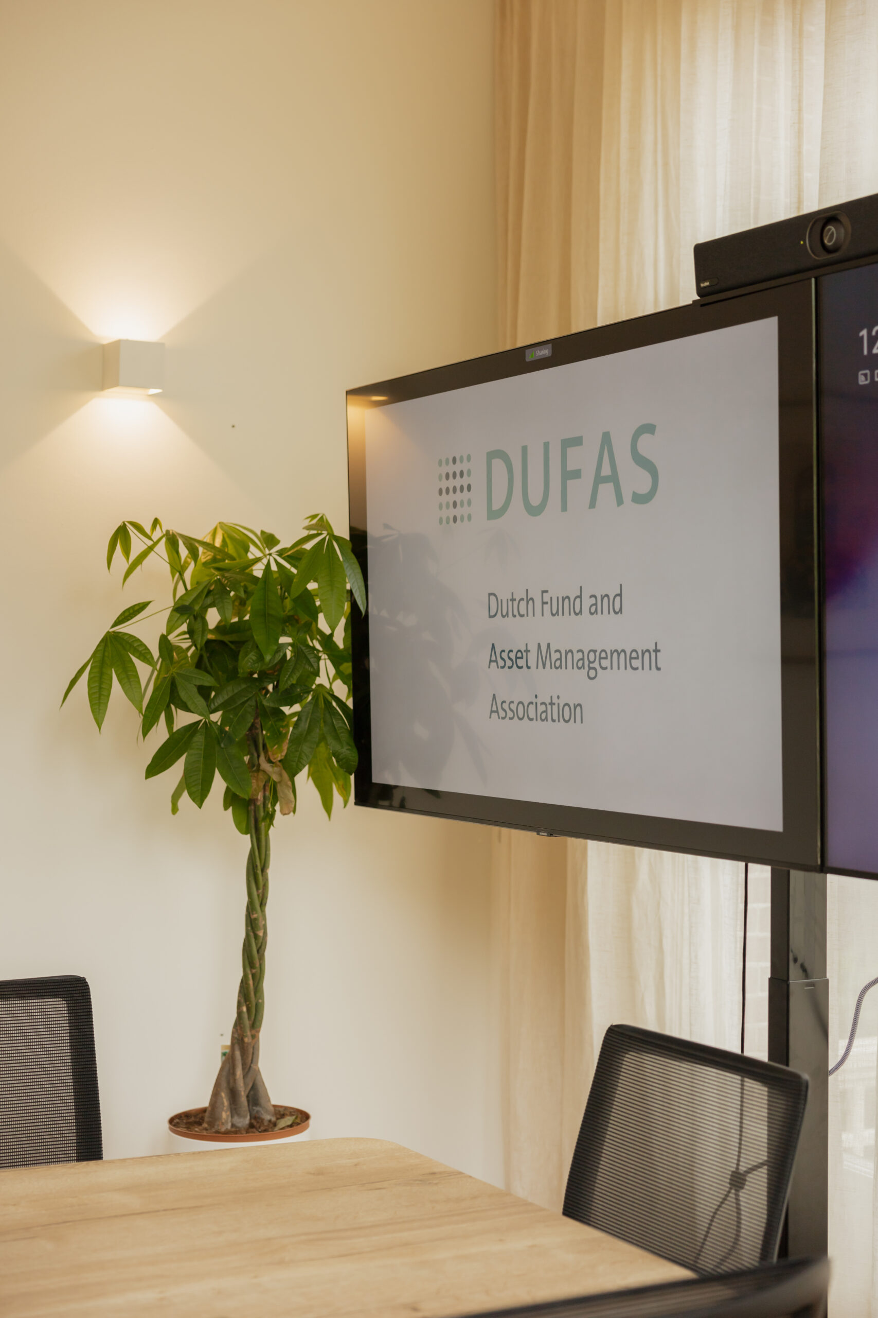 Vergaderruimte met een scherm waarop het logo en de naam van de Dutch Fund and Asset Management Association (DUFAS) te zien zijn.