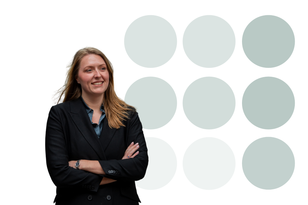 Vrouw in een donker pak lacht met gekruiste armen voor een achtergrond met negen groene cirkels.