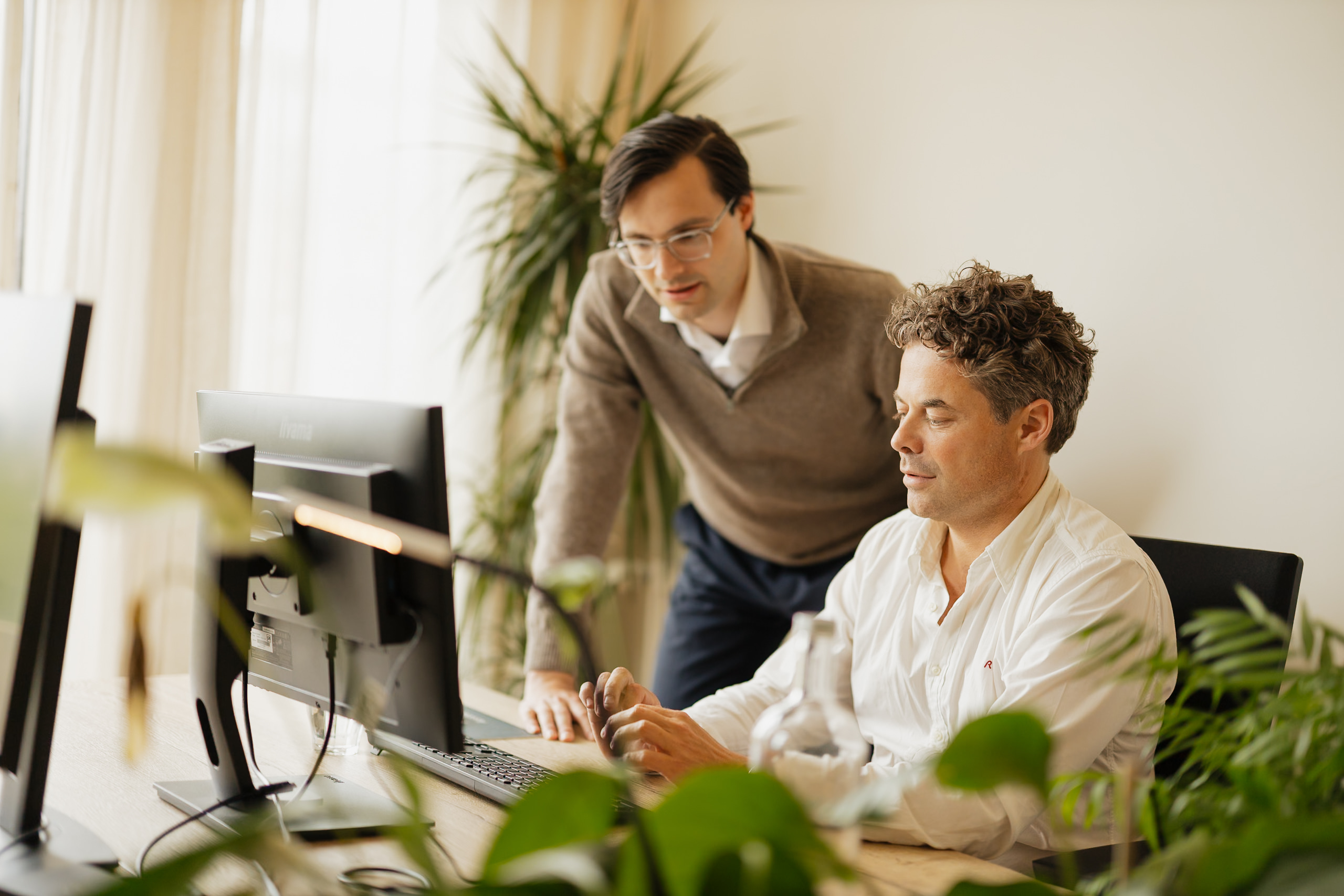 Twee mannen werken samen achter een computerscherm in een kantooromgeving bij de Dutch Fund and Asset Management Association.