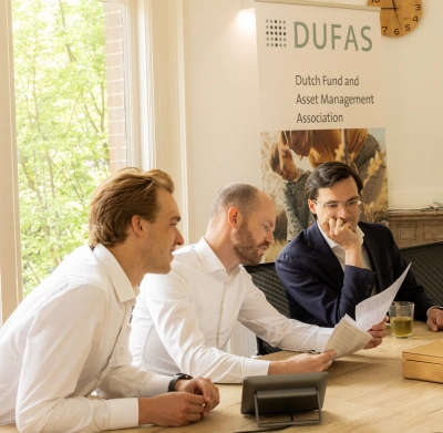 Drie mannen in overleg aan een vergadertafel bij DUFAS, met documenten en een drankje op tafel.