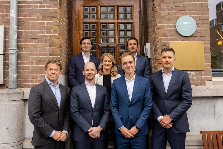 Groepsfoto van het DUFAS-team in pak voor het kantoorpand.