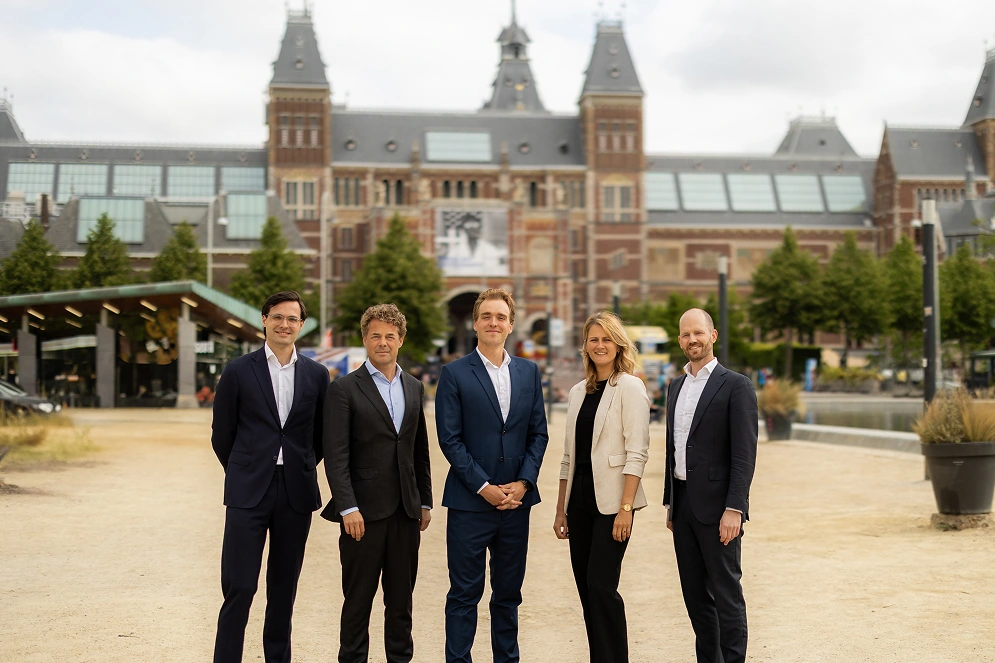 Vijf leden van het DUFAS-team poseren netjes gekleed op een plein voor het Rijksmuseum in Amsterdam.