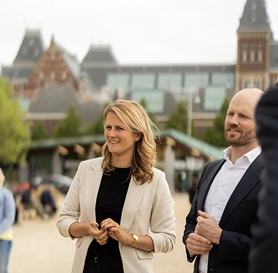 Manouk en Ron staan buiten in gesprek met het Rijksmuseum op de achtergrond.