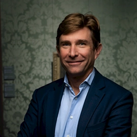 Portret van Damiaan, bestuurslid van DUFAS, in pak voor een decoratieve achtergrond.