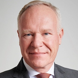Portret van Erik, bestuurslid van DUFAS, in pak met lichtgrijze achtergrond.
