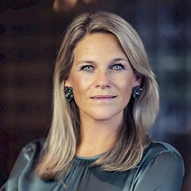 Portret van Karin, lid van het DUFAS-bestuur, met lang blond haar en een groene blouse.