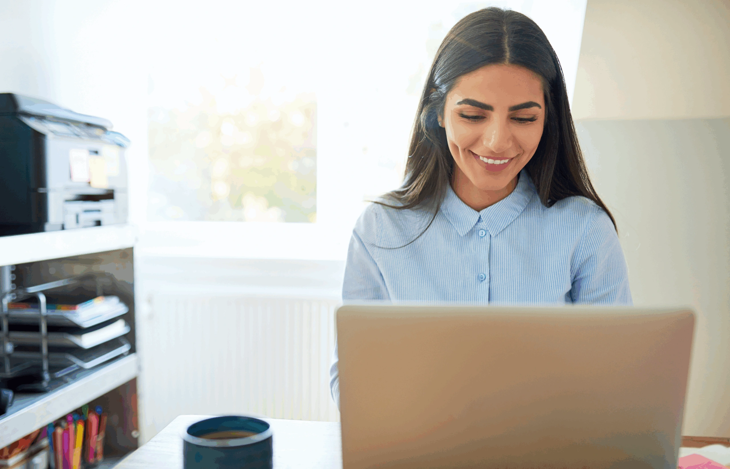 Vrouw glimlacht tijdens een online consultatie achter haar laptop in een lichte kantoorruimte.