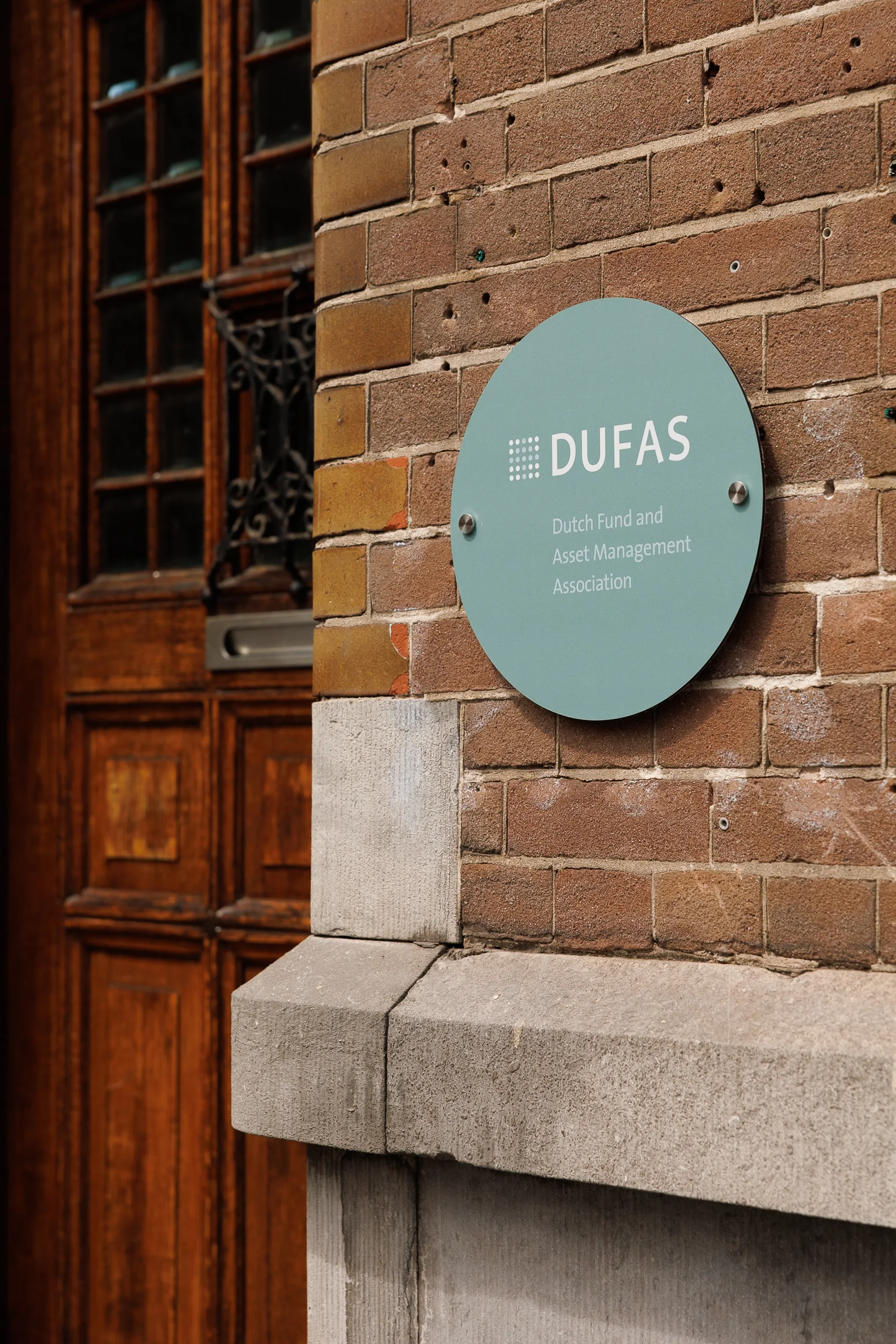 Een groen bord met het logo van de Dutch Fund and Asset Management Association (DUFAS) op een bakstenen muur.