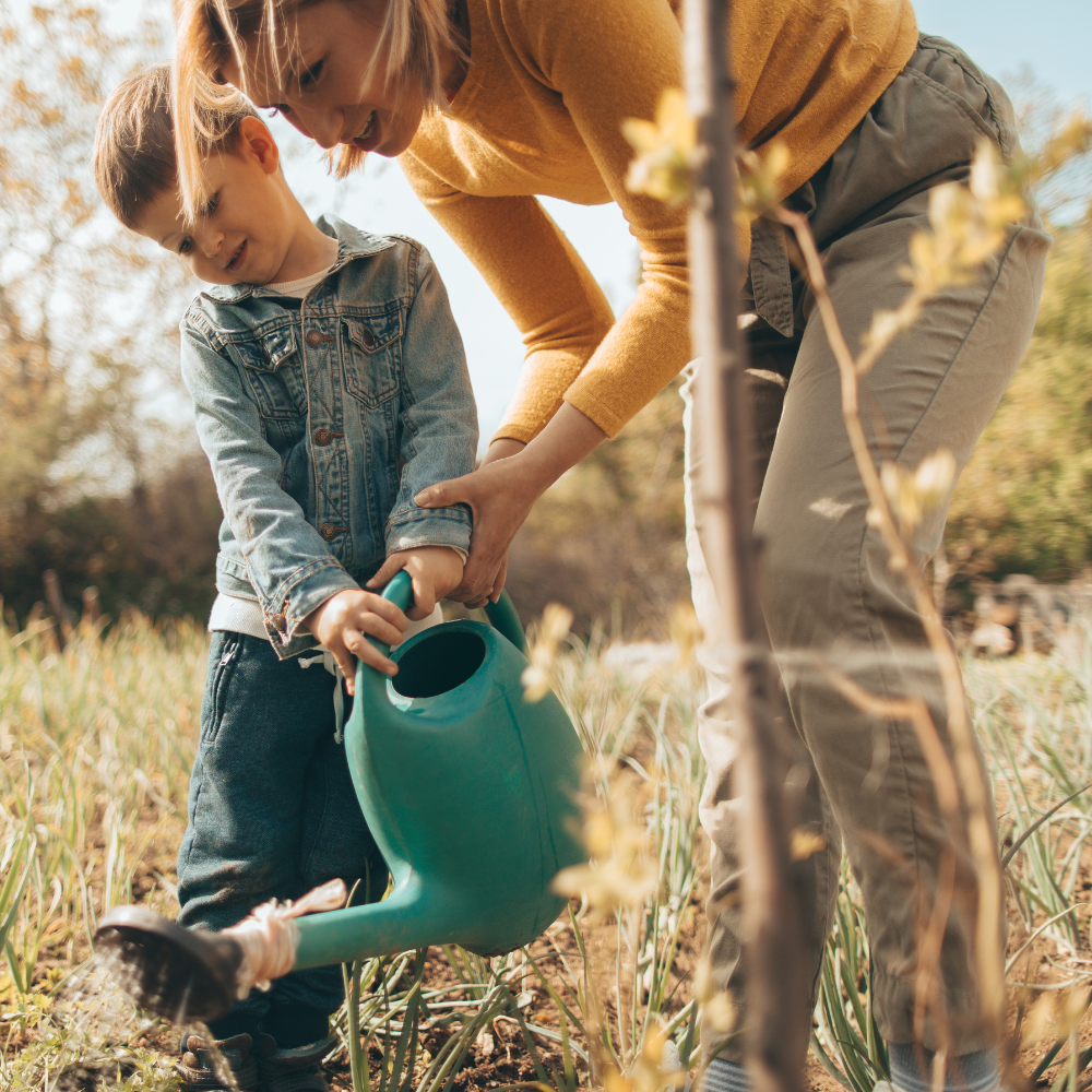 Vrouw en kind geven samen water aan planten in een moestuin als onderdeel van een leefbare wereld.