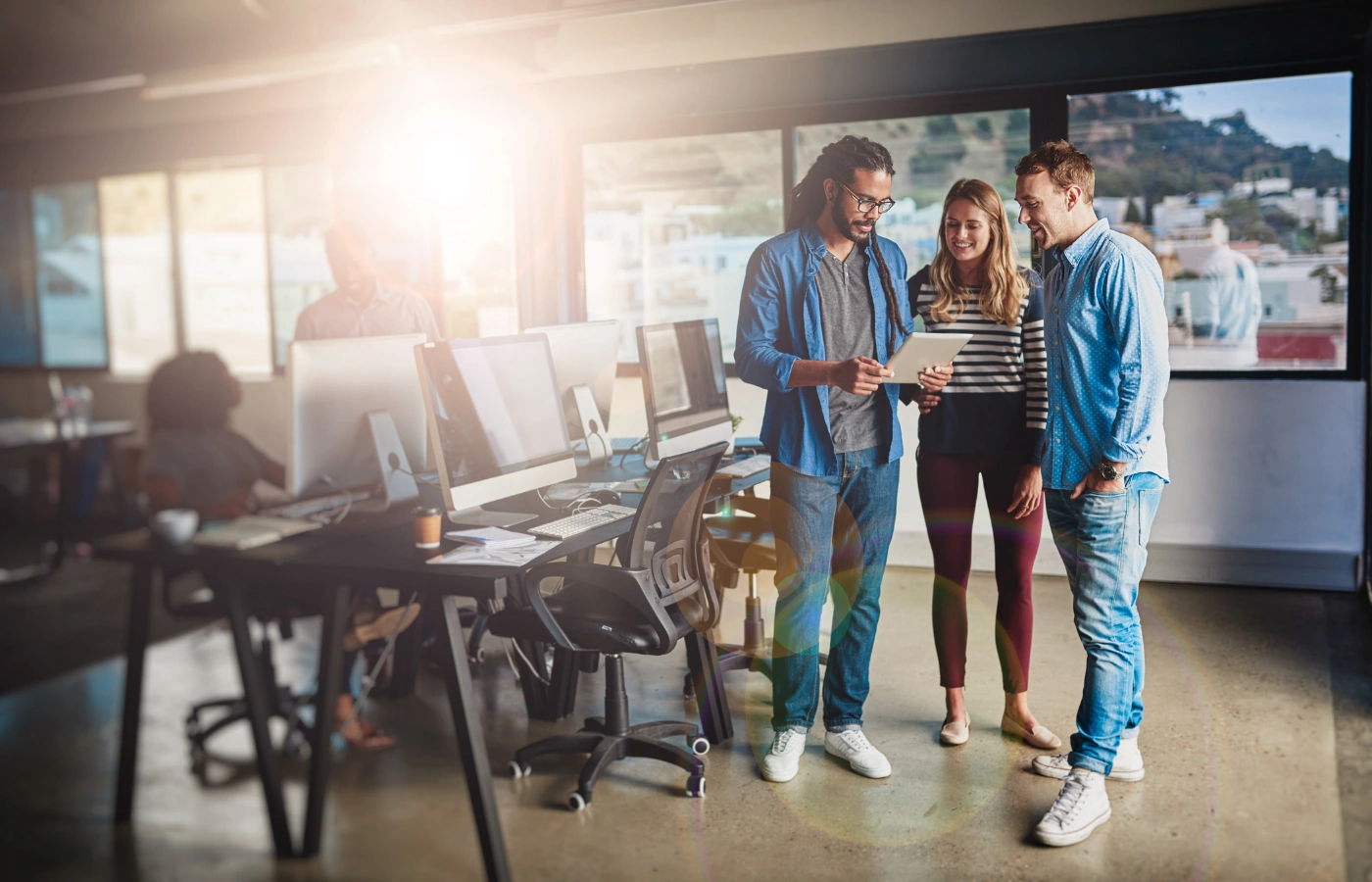 Drie jonge professionals overleggen met een tablet in een modern kantoor, symbool voor een sterke samenleving en economie.